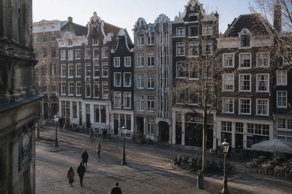 A row of narrow Amsterdam canal houses with gabled facades along a quiet morning street