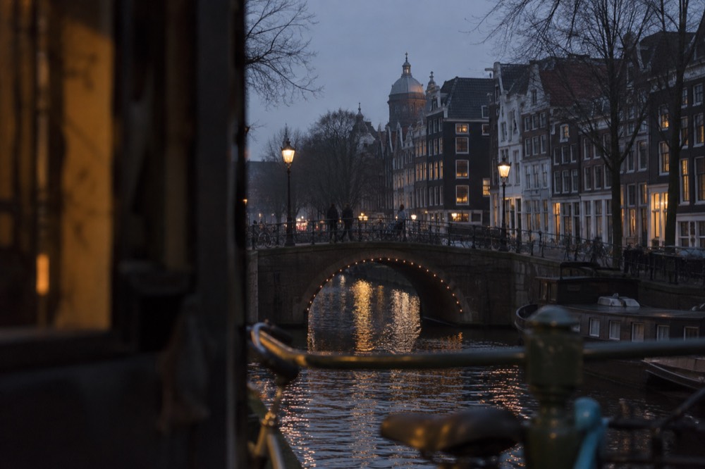 Narrow Amsterdam street with canal houses and bicycles leaning against a bridge railing