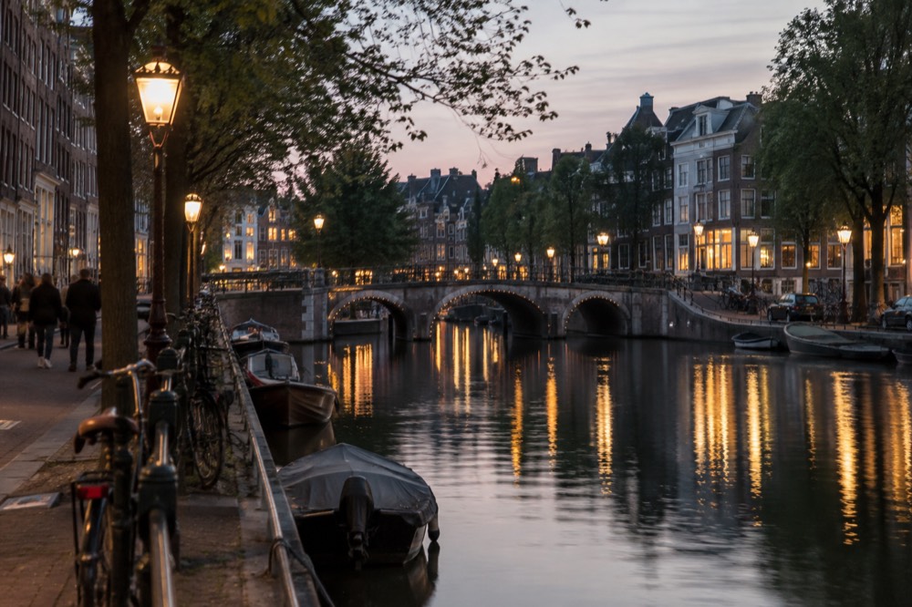 A canal at dusk with historic street lamps reflected in the still water