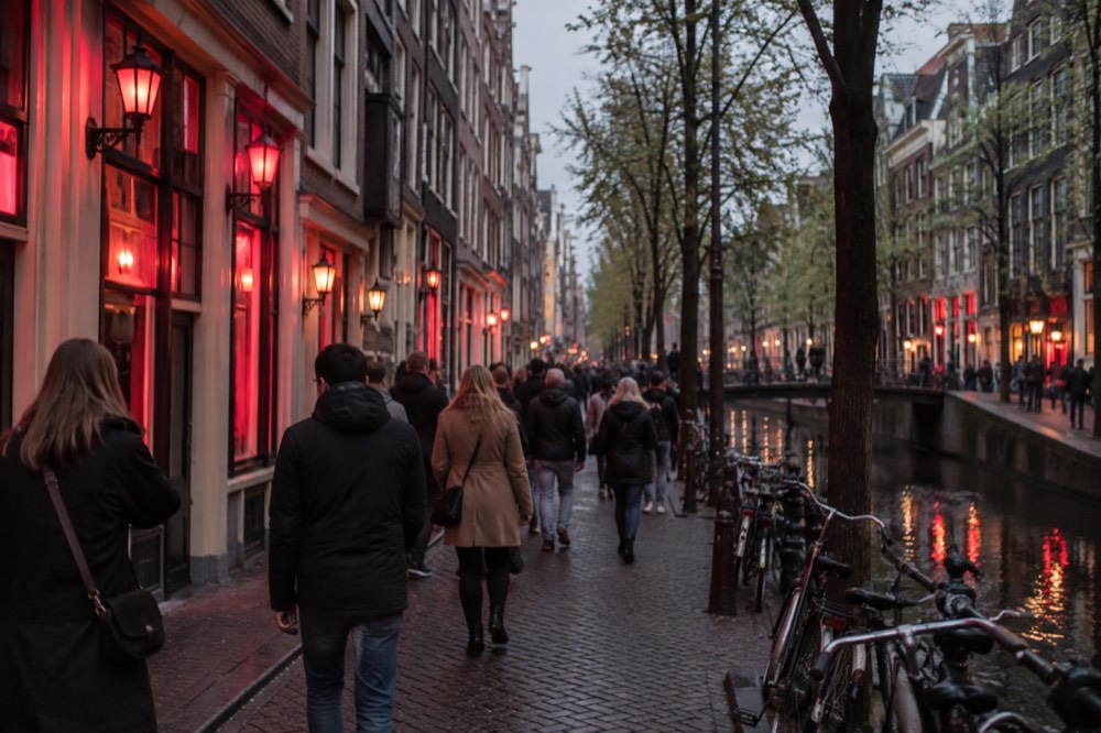 Crowded narrow Amsterdam street lit by red lamps and neon signs in the evening
