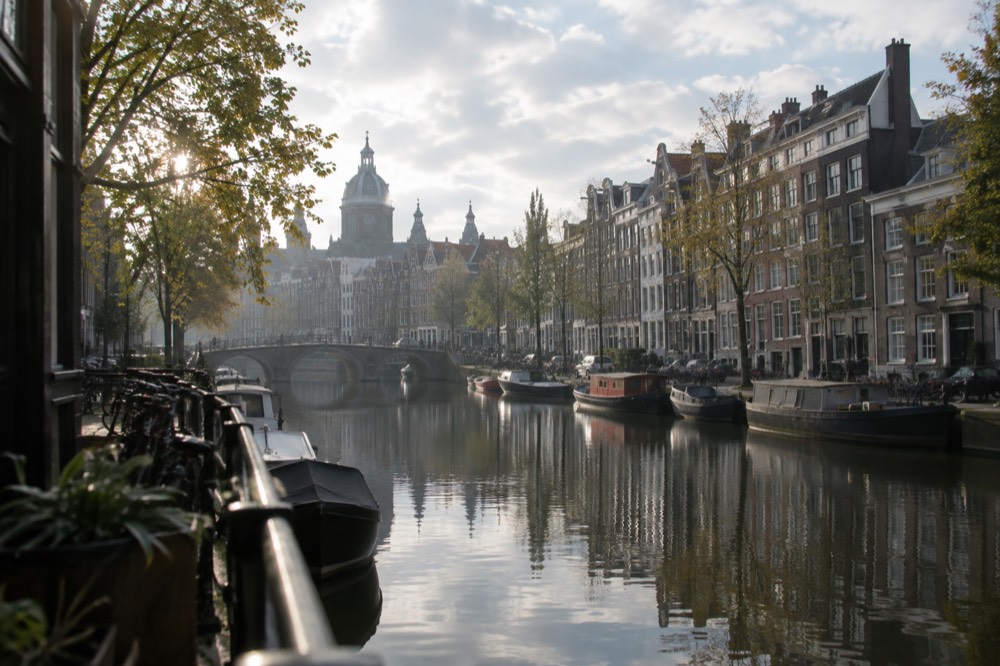 Wide canal lined with tall narrow houses reflected in still water in the early morning