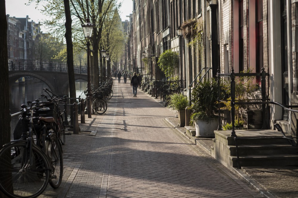A calm Amsterdam street of brick townhouses with bicycles parked against railings in soft morning light