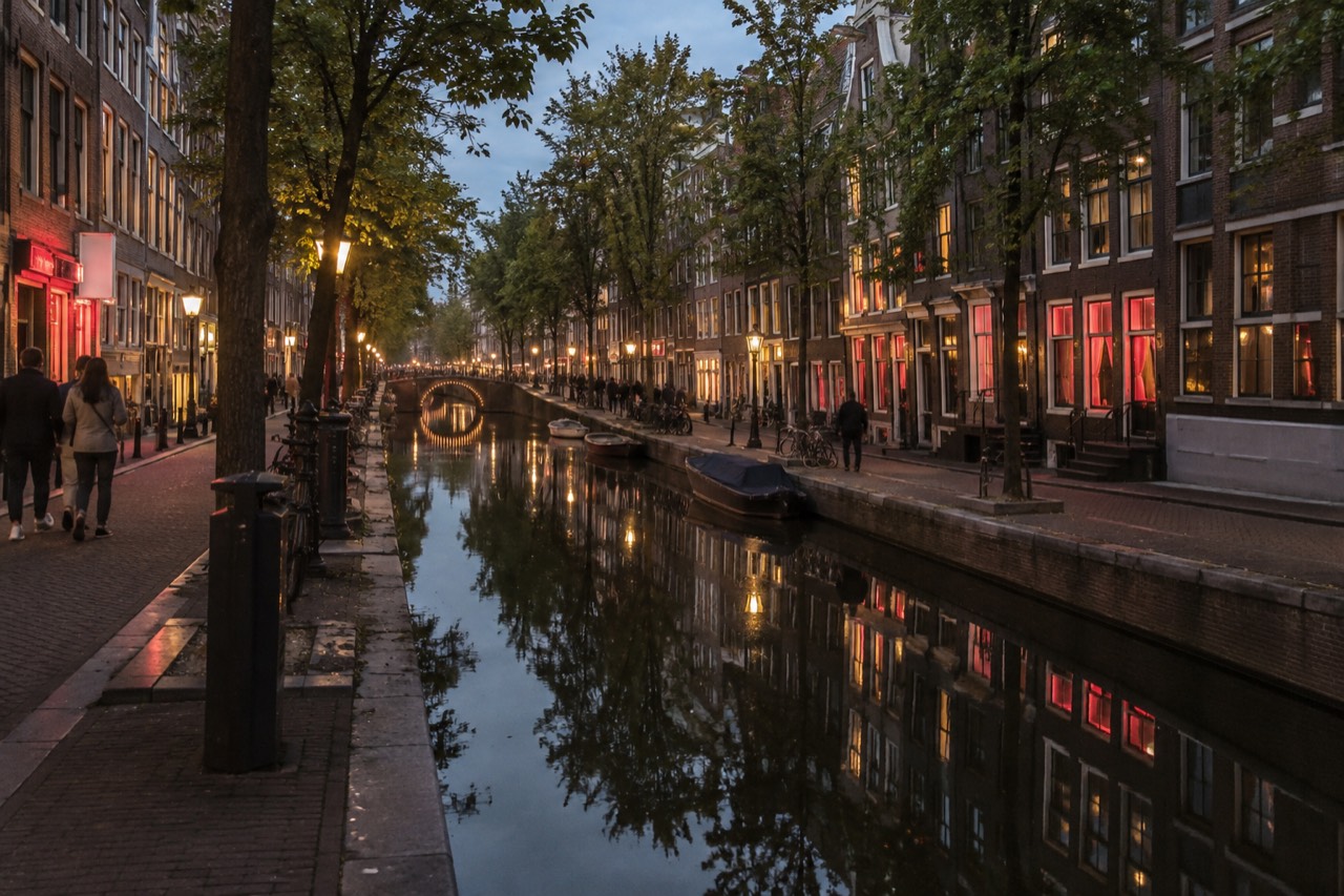Evening view of a quiet Amsterdam canal lined with narrow brick houses and trees reflected in still water