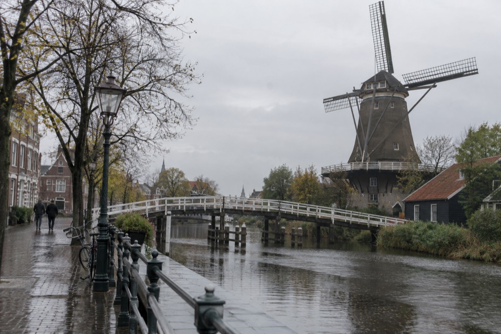 A traditional Dutch windmill with turning sails beside a wooden bridge over a narrow river