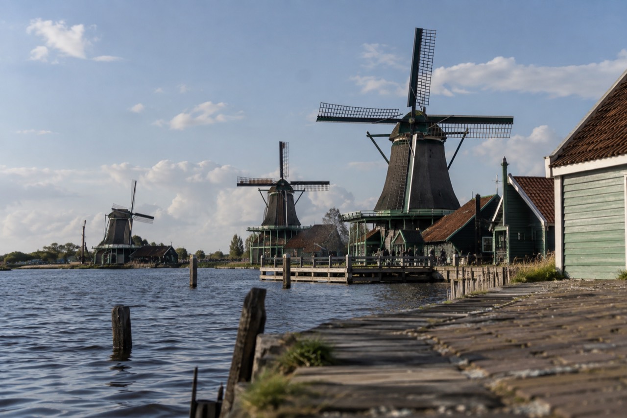 A row of historic Dutch windmills standing beside a waterfront with green wooden houses
