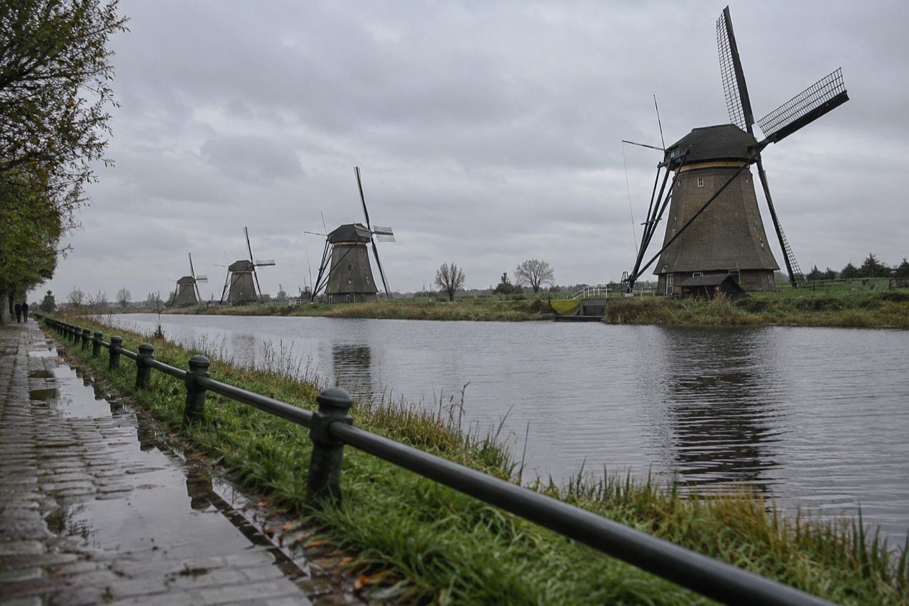 Row of historic windmills standing along a canal with green fields behind them