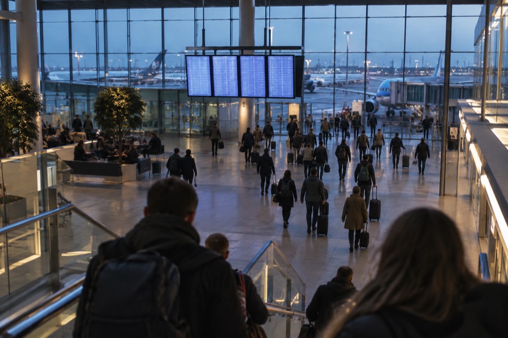 A departures hall at Schiphol Airport with travellers and flight information screens