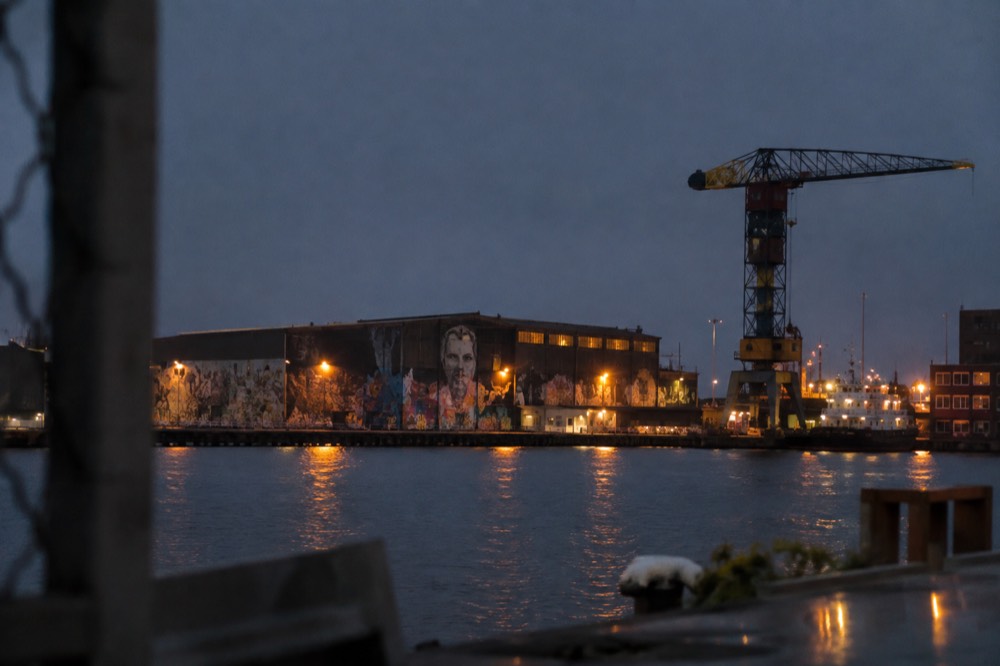 Graffiti-covered warehouse walls and a crane at NDSM Wharf seen across open water