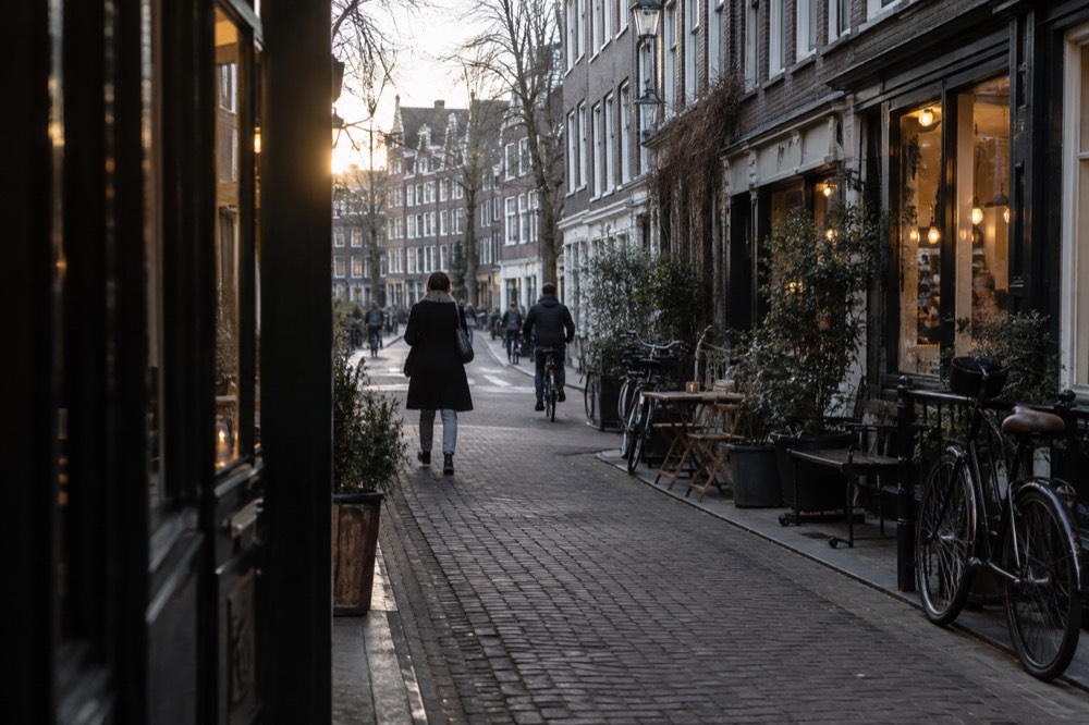 A narrow brick street of terraced houses with bikes locked to railings and café windows lit in the evening