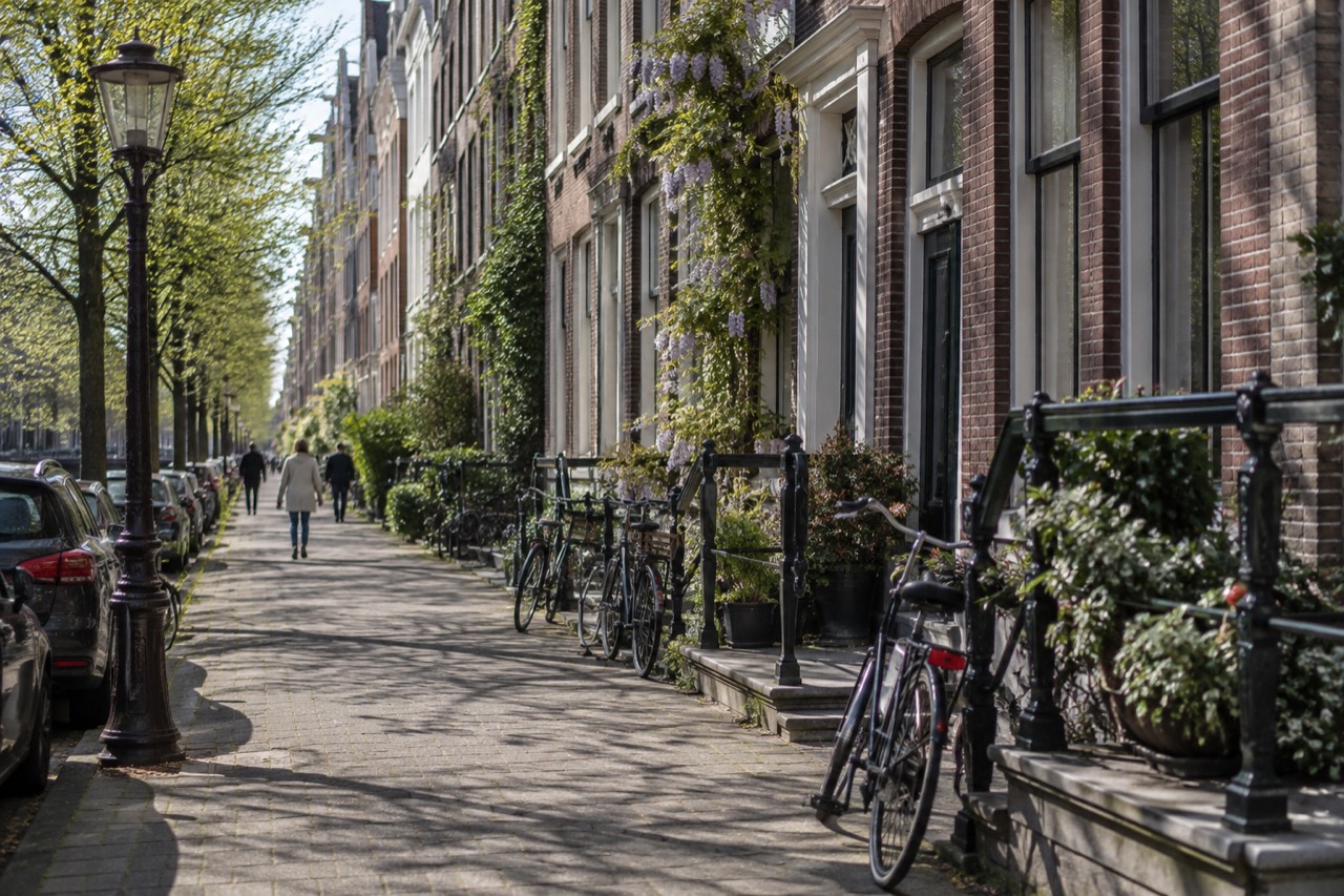 Rows of narrow brick terraced houses along a quiet street in De Pijp with bicycles parked against railings