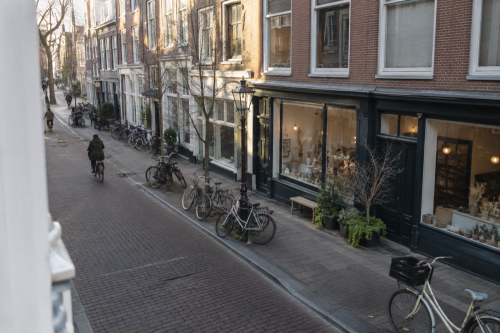 A shopfront on a wide Amsterdam street with bicycles parked along the kerb