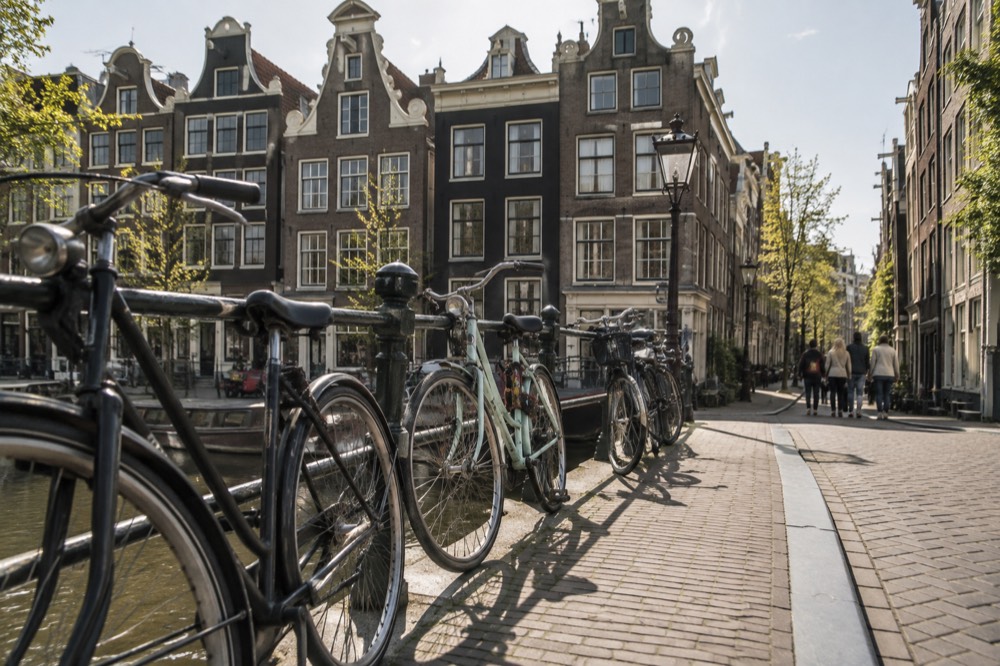 Row of narrow gabled canal houses along a quiet Jordaan street with bicycles leaning on a bridge