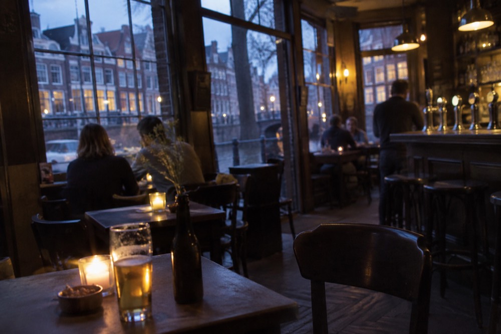 Small traditional Dutch café interior with dark wooden tables and a bar with beer taps