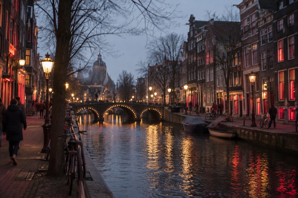 Evening view of a canal in the old centre of Amsterdam with illuminated bridge and tall narrow houses