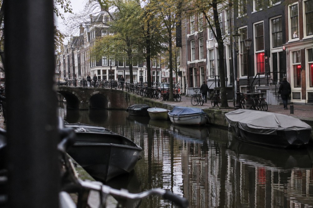 Canal boats moored along a burgwal waterway with old Amsterdam facades reflected in the water