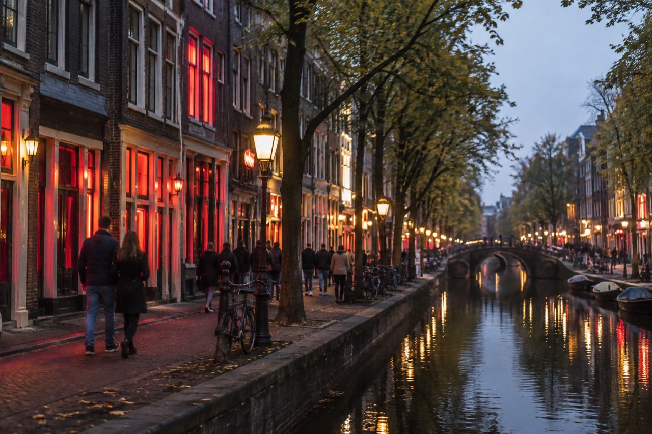 Narrow Amsterdam canal street at dusk with old gabled buildings and warm lamplight