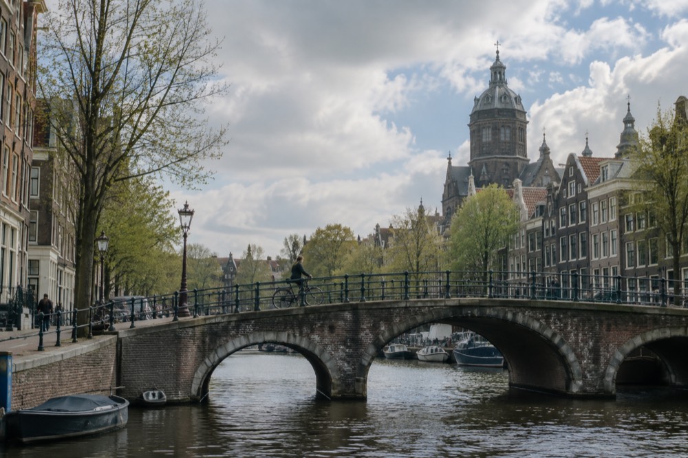 A cyclist crossing a small arched bridge over an Amsterdam canal