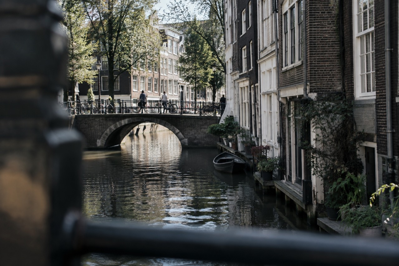 Canal-side shopfronts and a stone bridge along a quiet Amsterdam side street