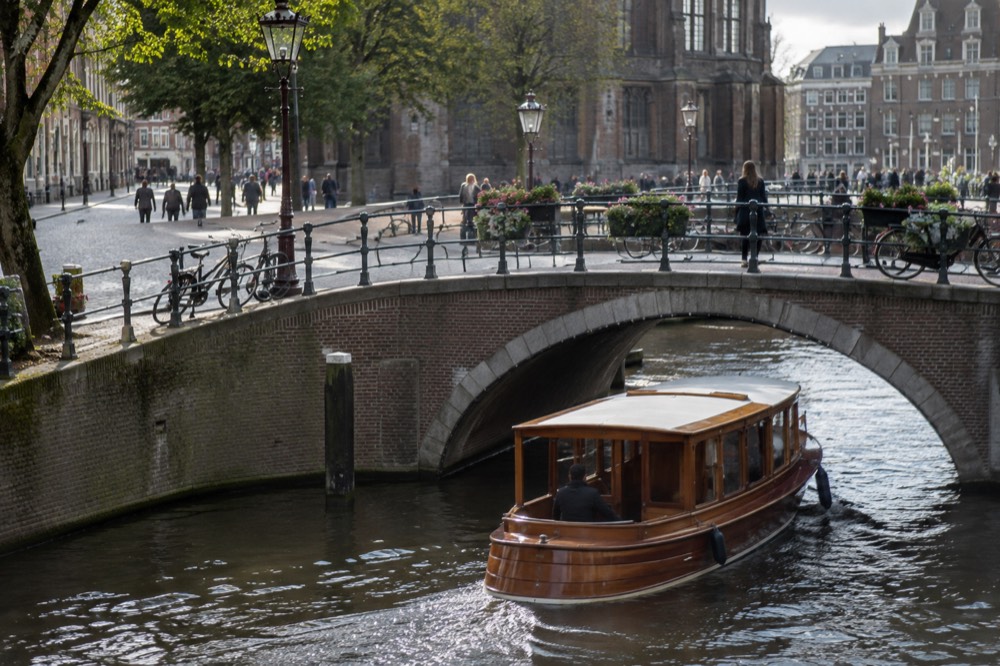 Classic wooden saloon boat gliding under a brick bridge on an Amsterdam canal