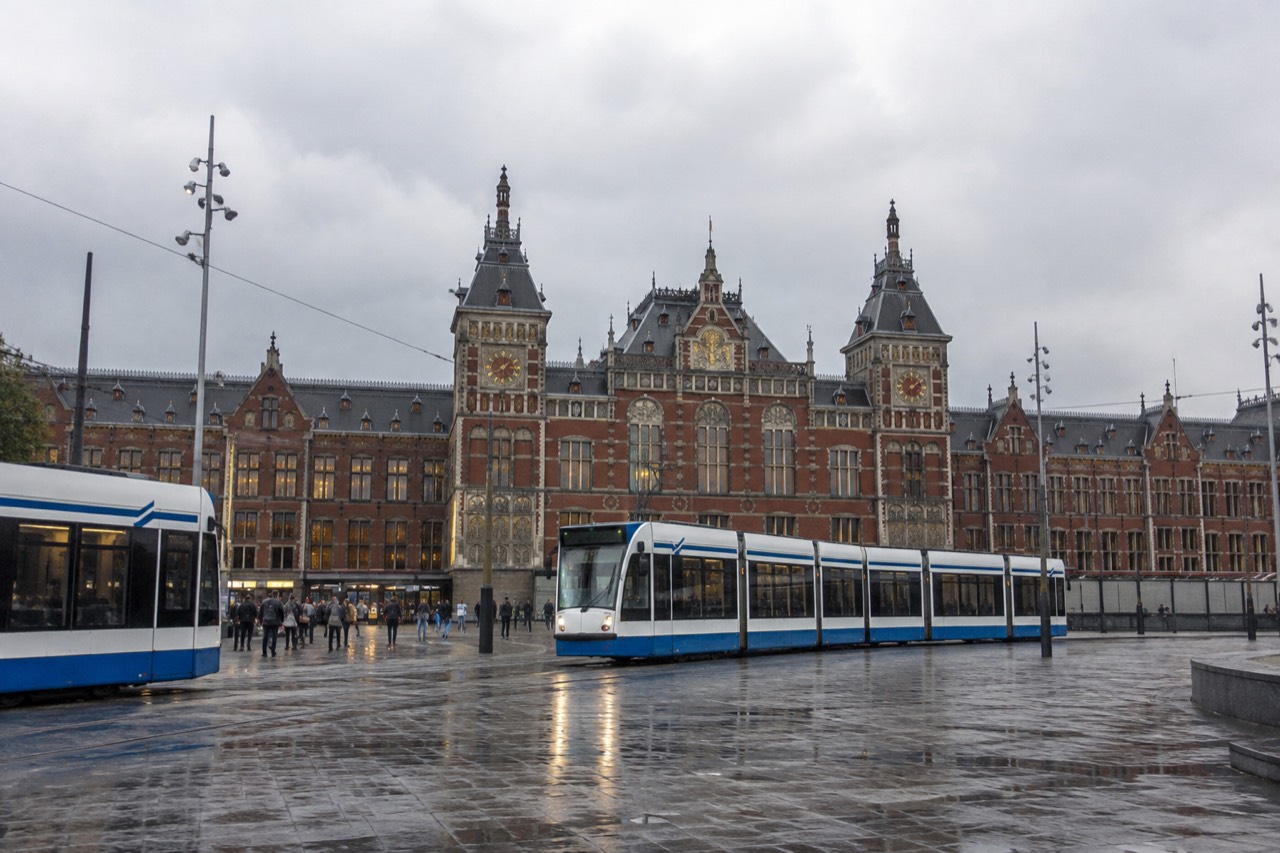 The brick facade of Amsterdam Centraal Station seen from the station square with trams in the foreground