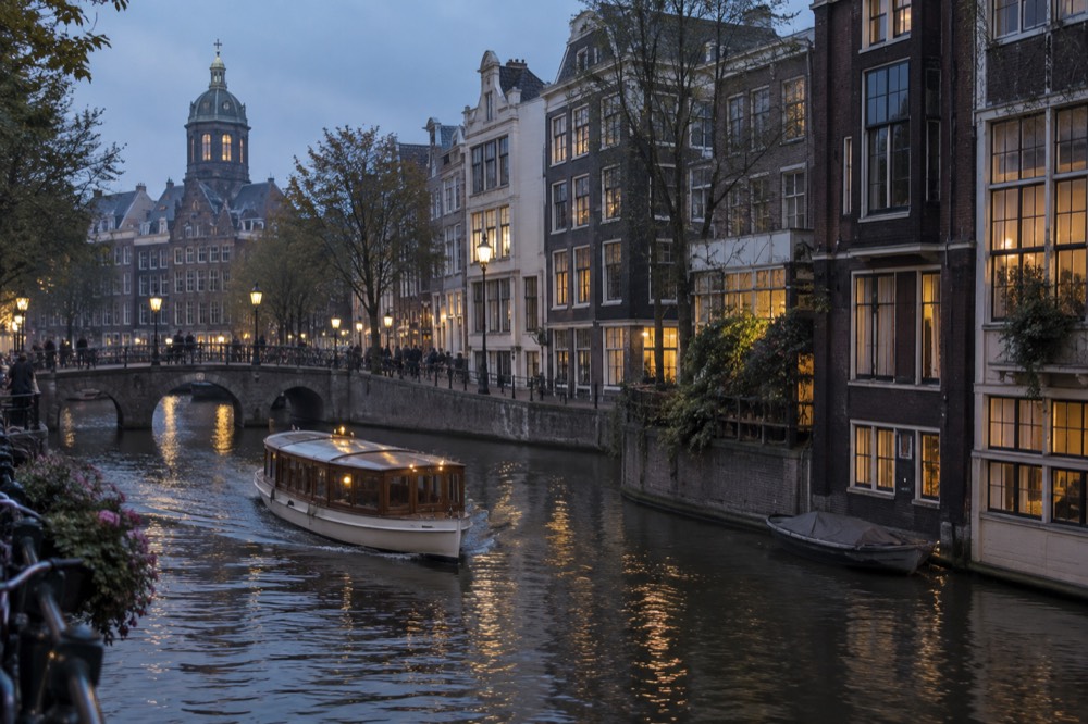 A traditional Amsterdam saloon boat passing narrow canal houses at dusk