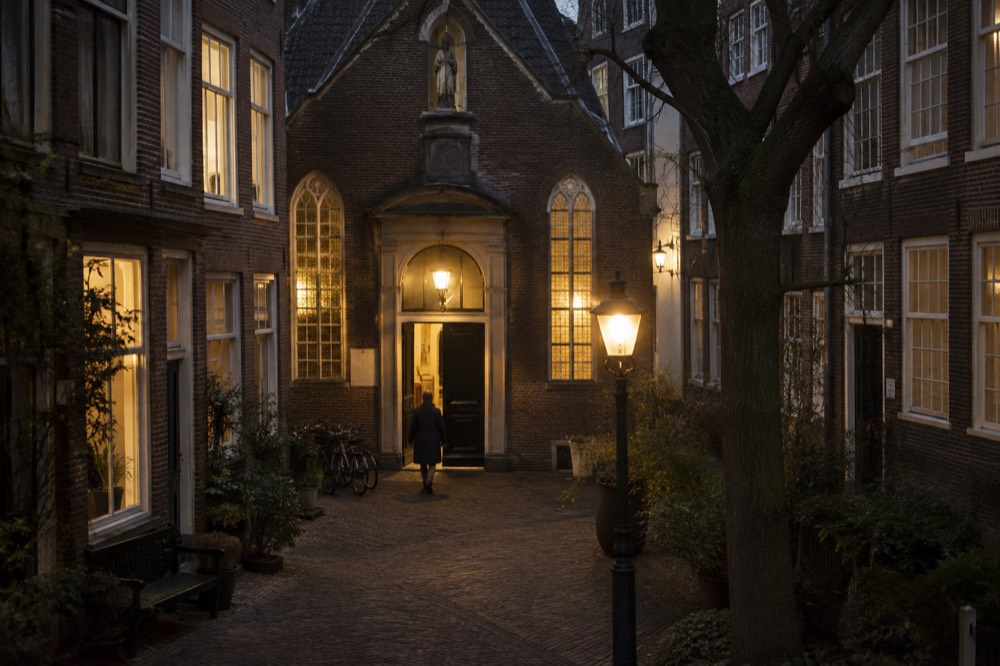 A small chapel entrance set between tall brick houses in an enclosed Amsterdam courtyard