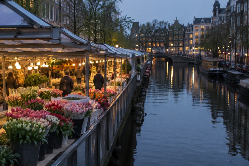 A covered market walkway beside a canal with flower stalls in spring