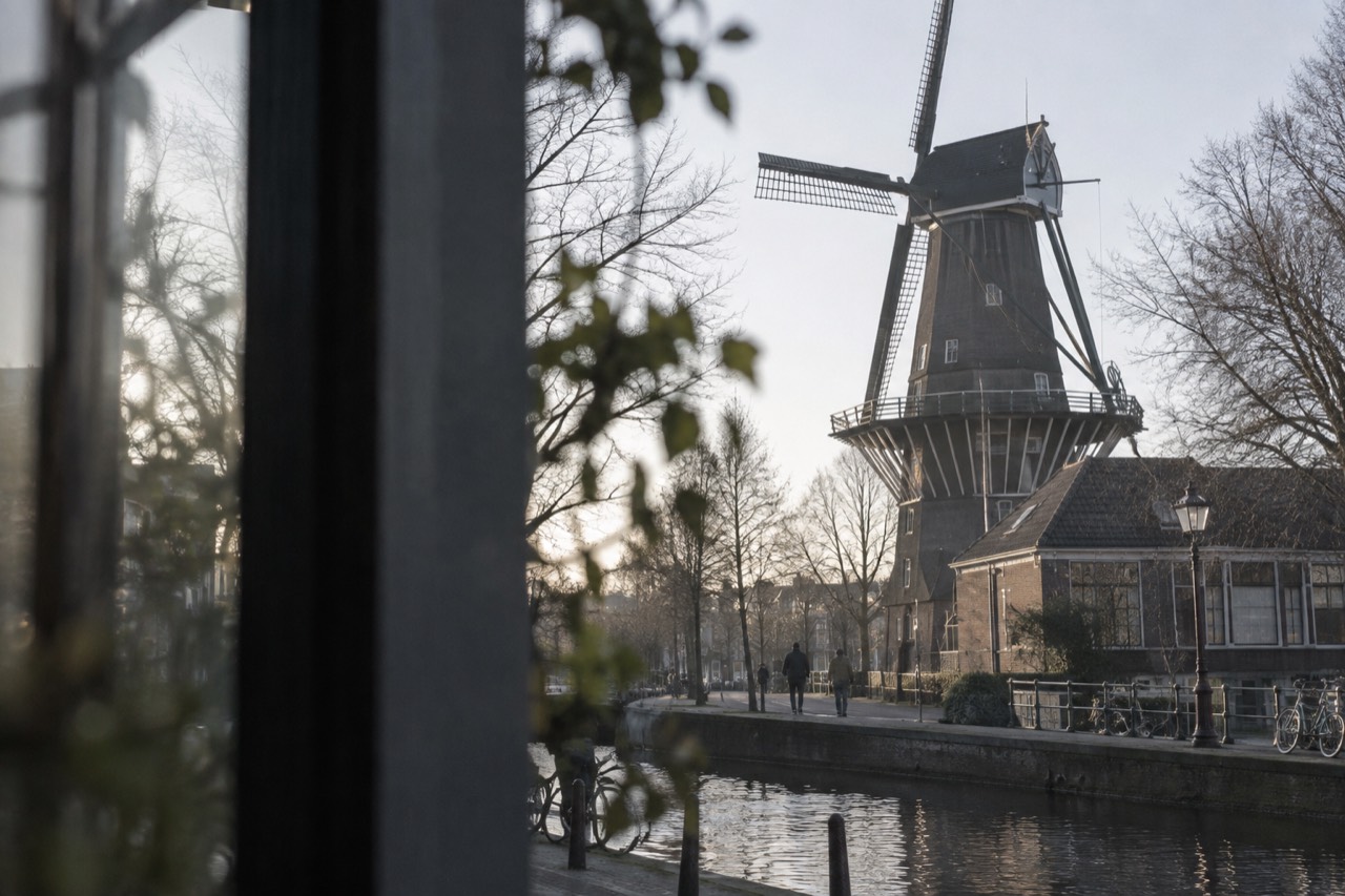A tall wooden windmill beside a low brewery building on a quiet Amsterdam street