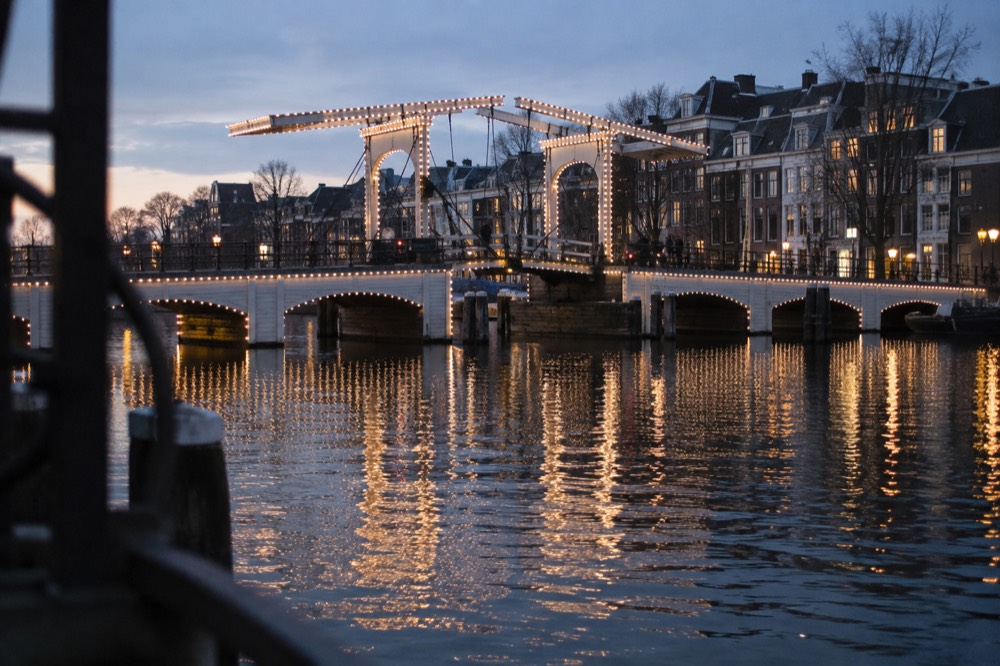 Strings of white lights along the timber of the Magere Brug reflected in the Amstel at night