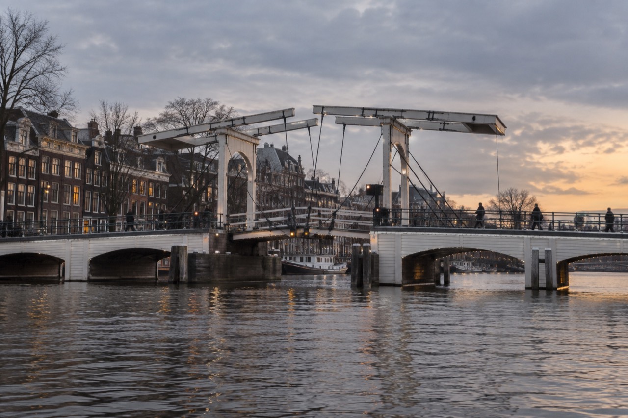 A white wooden drawbridge over the Amstel river at dusk with canal houses behind it
