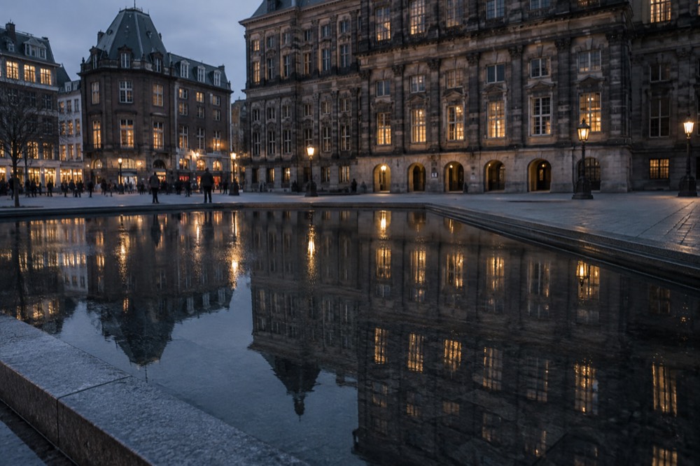 A museum facade reflected in a shallow pool of water on a city square at dusk
