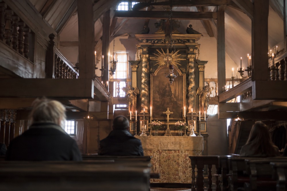 A candlelit hidden church interior with wooden galleries and a gilded altar inside an attic