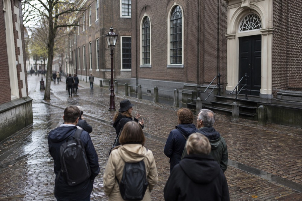 A guide speaking to a small group of visitors on a cobblestone street lined with old brick buildings