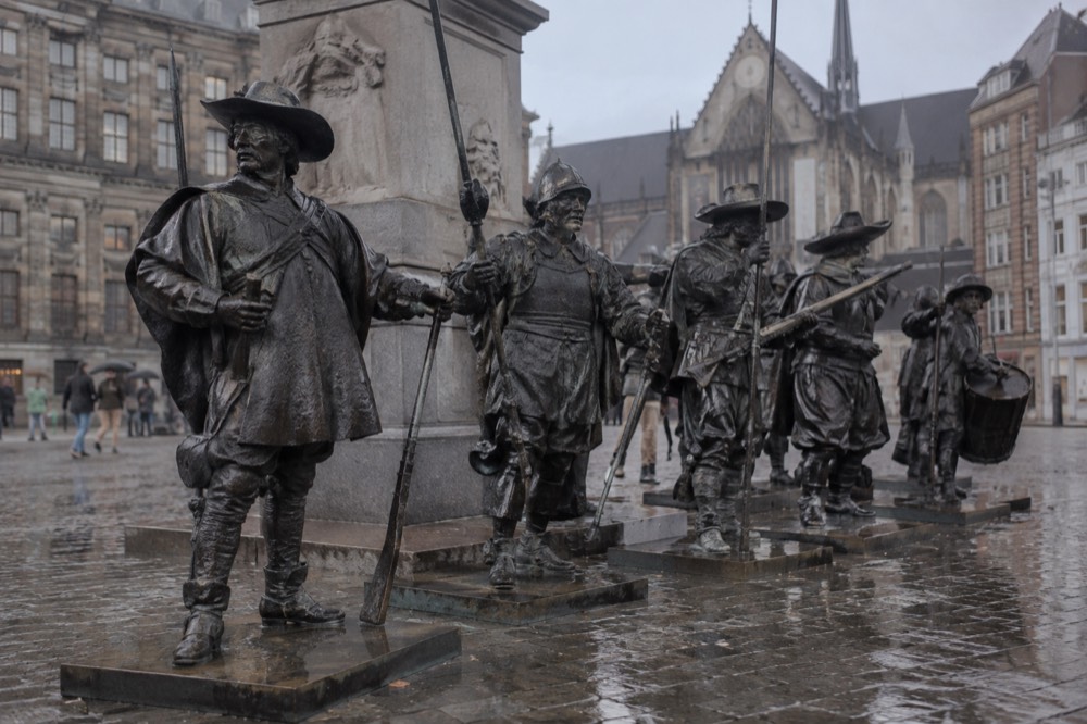A bronze sculpture group of armed period figures standing in a row on a square near a stone pedestal