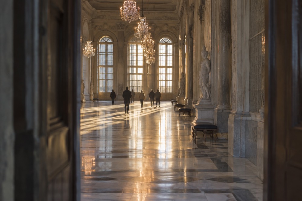 Long hall with marble floors, chandeliers and tall windows