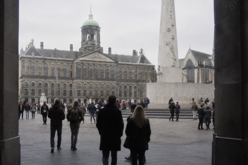 Crowded paved square with a large monument and classical building behind