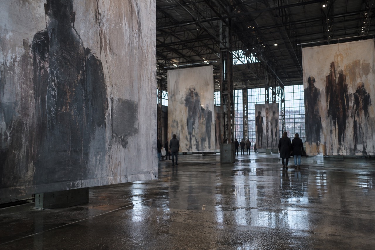 Large warehouse interior with oversized murals painted on canvas hung from steel beams