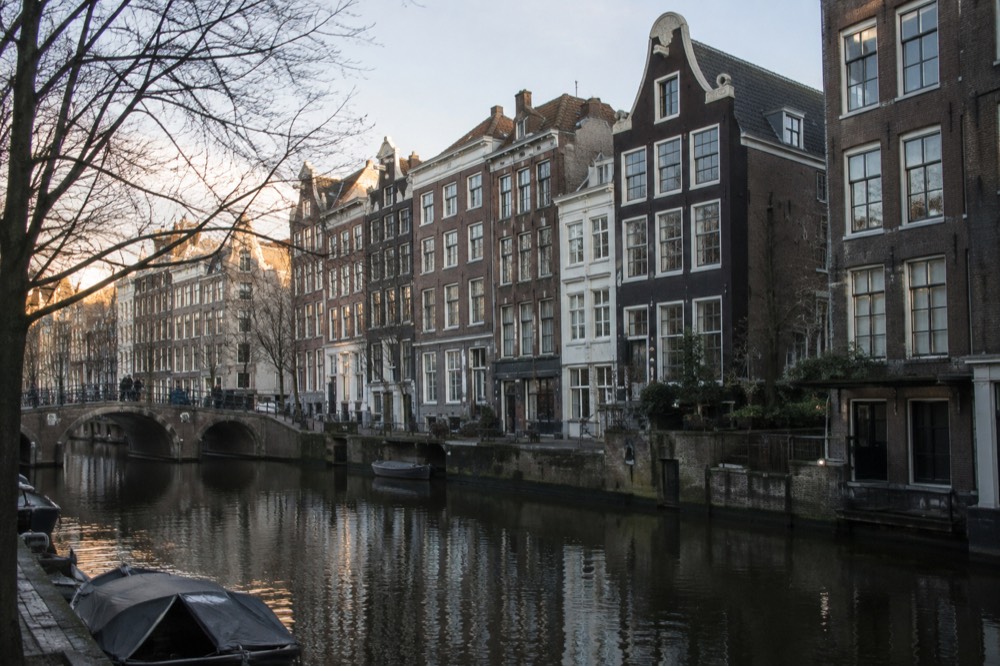 A narrow medieval canal house facade on the Singel in Amsterdam beside dark water