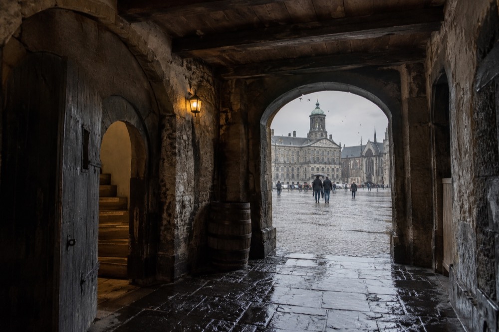 A dim stone cellar corridor with heavy wooden beams and low arched doorways