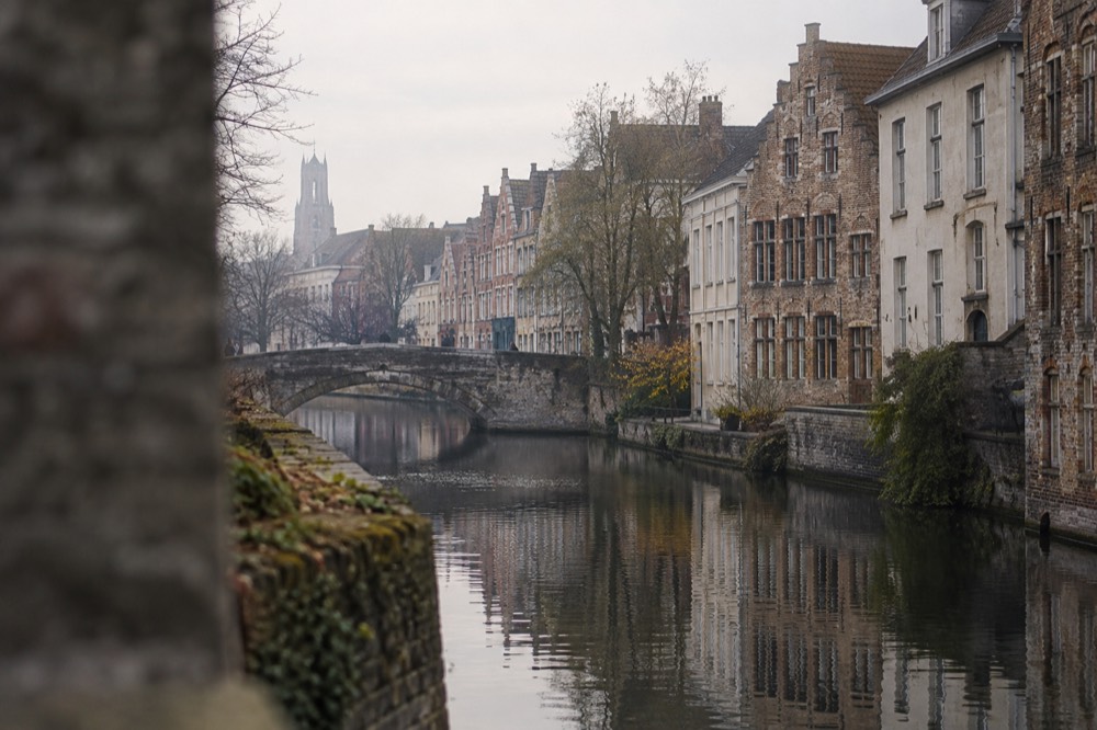 A calm canal in Bruges with stone bridges and stepped brick facades along the water