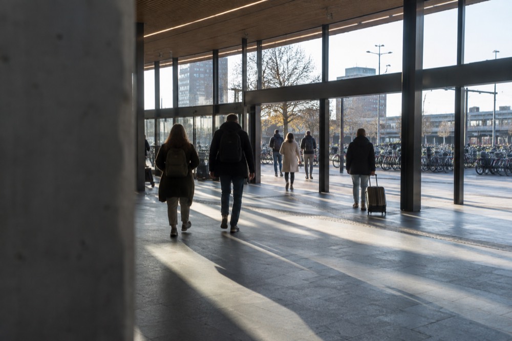 Modern Delft station hall with travellers walking toward the exit and bicycles parked outside