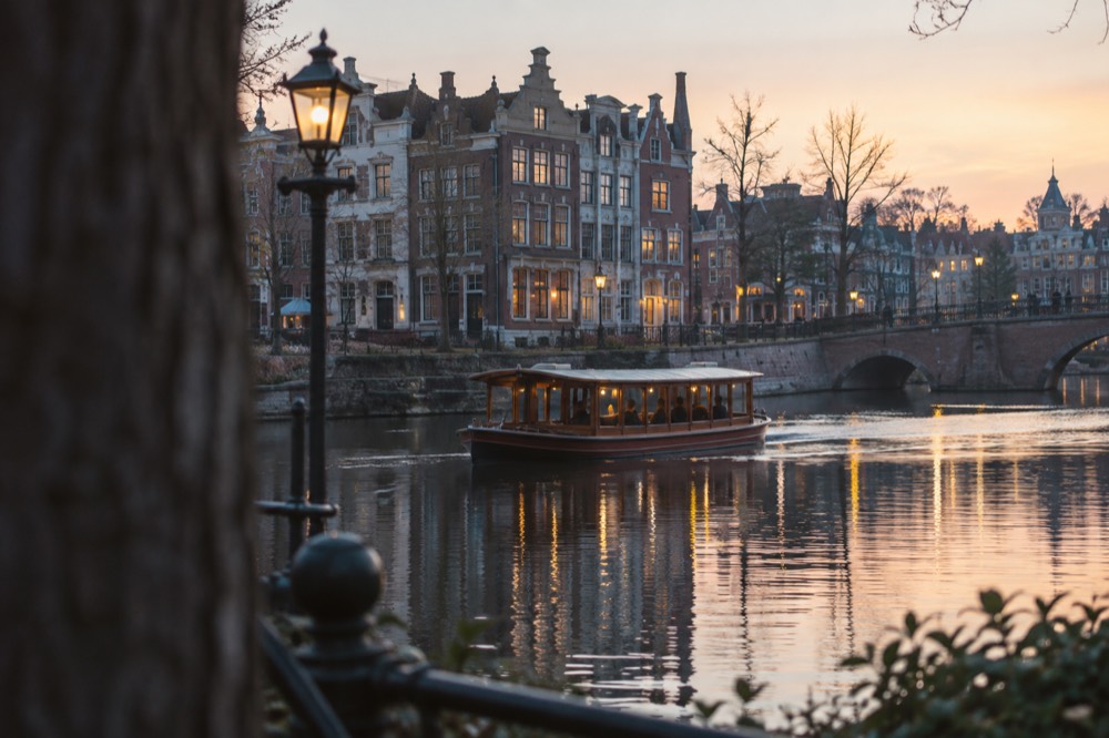 Amsterdam canal houses reflected in the water at dusk with a classic saloon boat passing