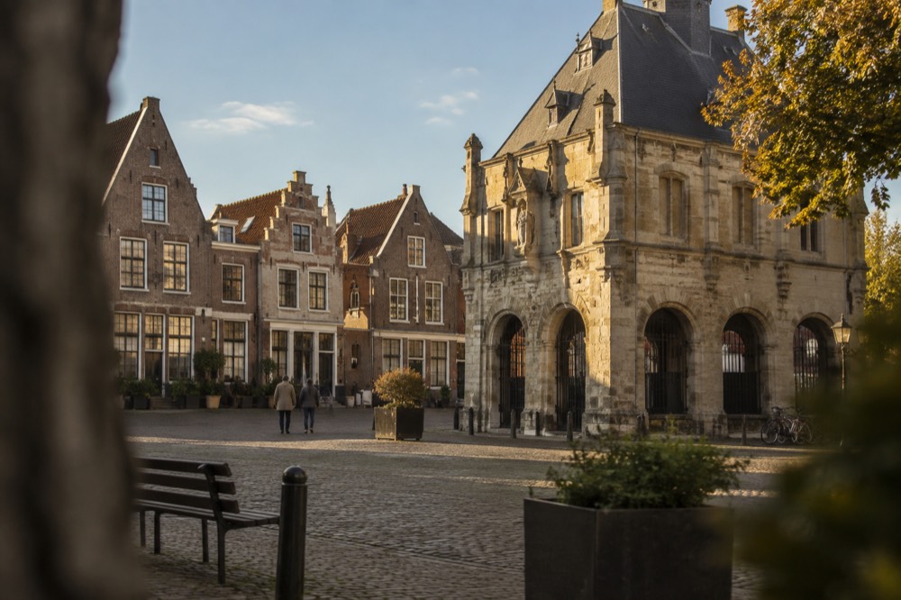 A quiet town square with historic Dutch buildings and a stone weigh house under a blue sky