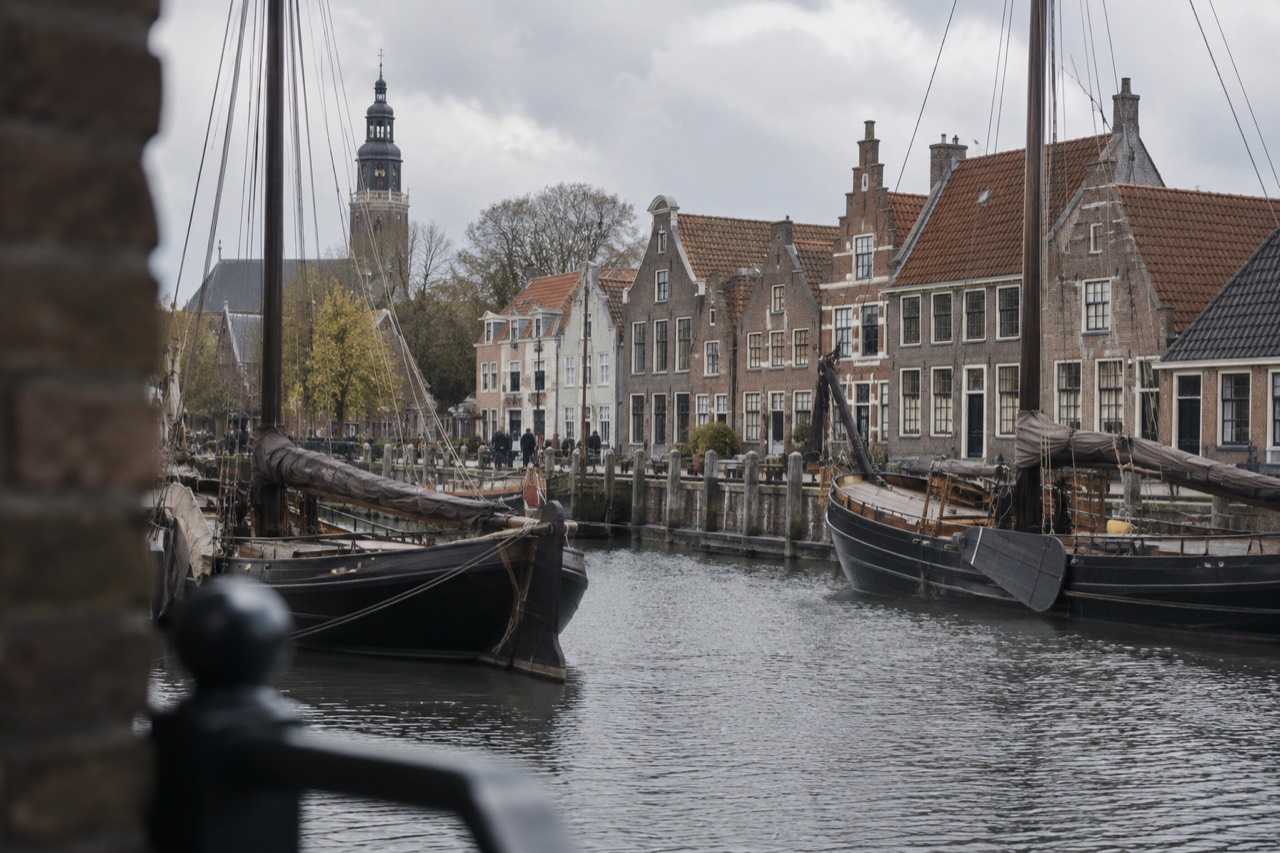 Historic gabled houses beside a harbour with old sailing ships moored along the quay