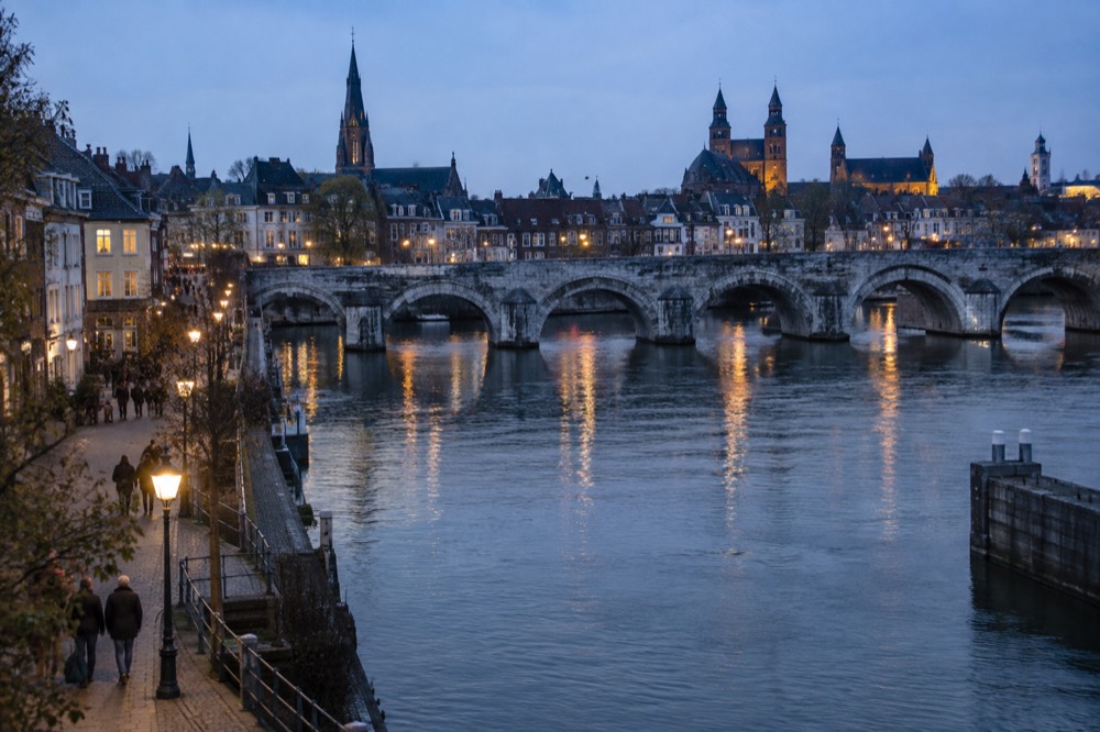 Old stone bridge over the Maas river with the Maastricht skyline of towers behind
