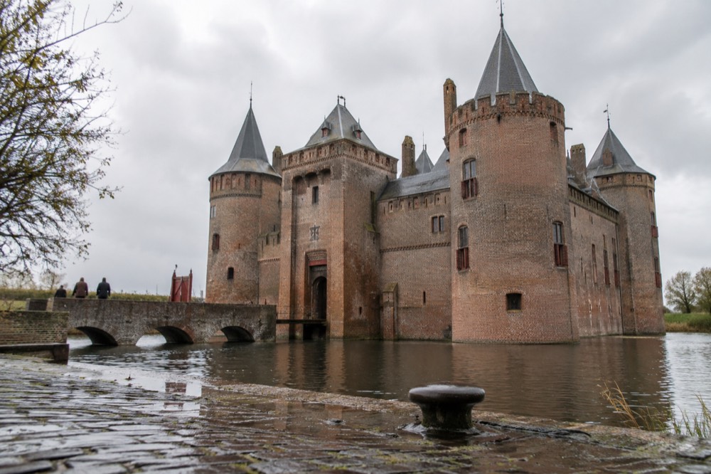 A red brick castle with twin round towers standing behind a wide water moat