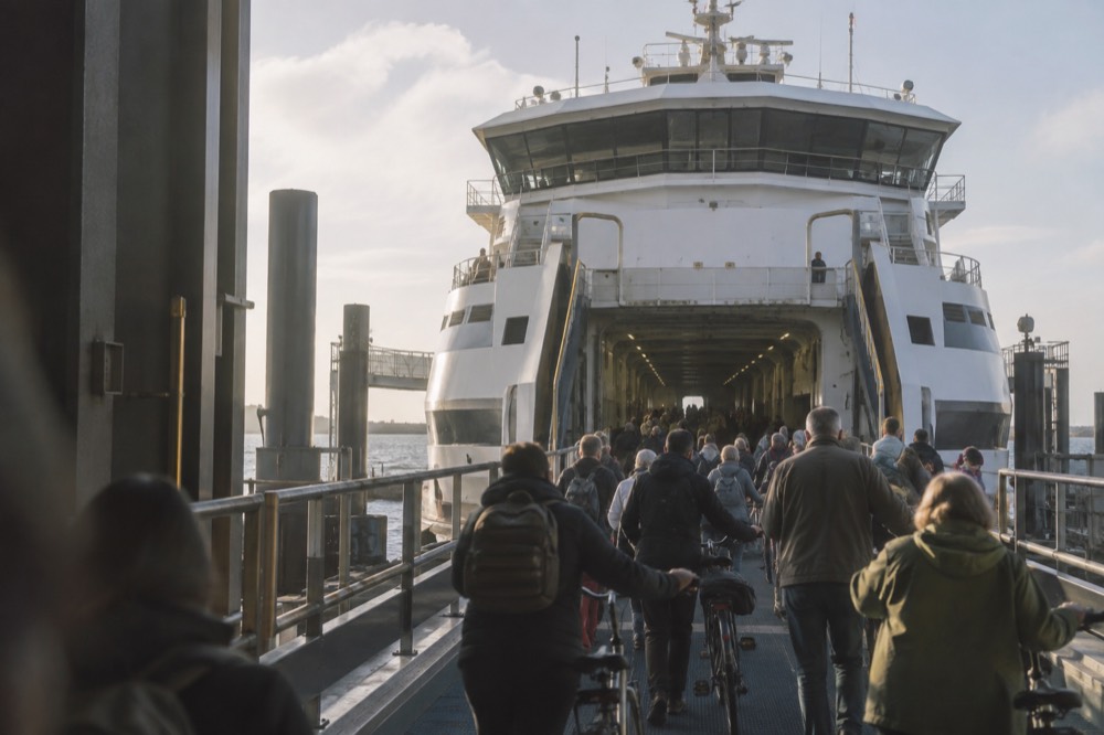 A ferry at a Dutch terminal with cyclists and walkers boarding in the foreground