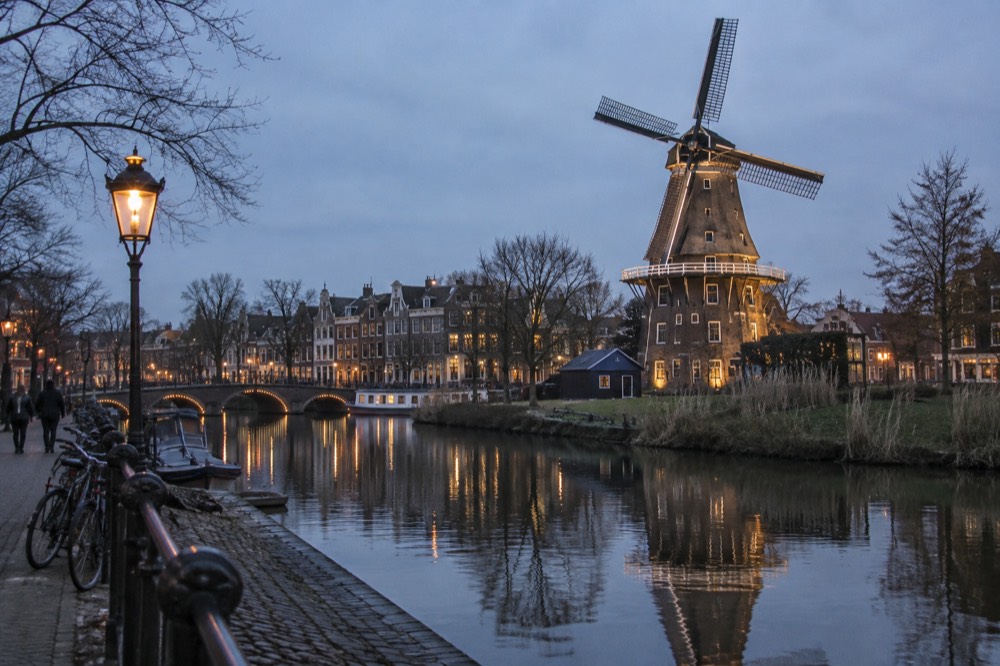 A traditional Dutch windmill with a thatched roof reflected in a still canal