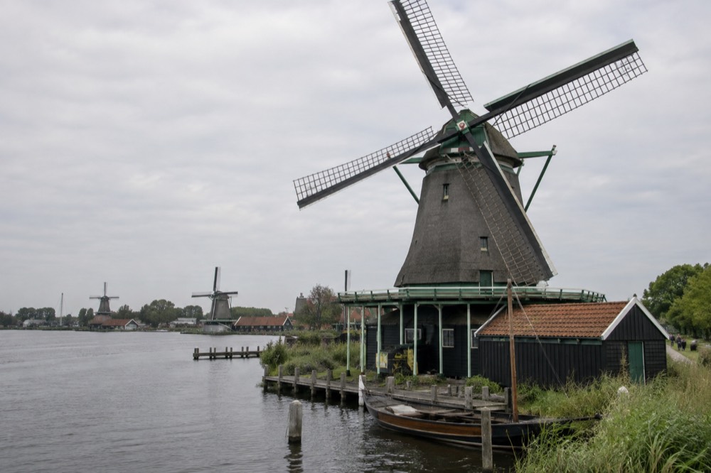 Close view of a traditional Dutch windmill with turning sails beside a river, wooden boat moored below