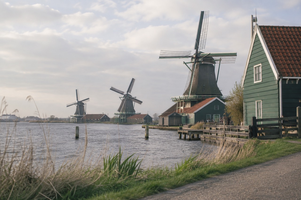 Row of historic Dutch windmills along a river bank at Zaanse Schans with wooden houses in the foreground
